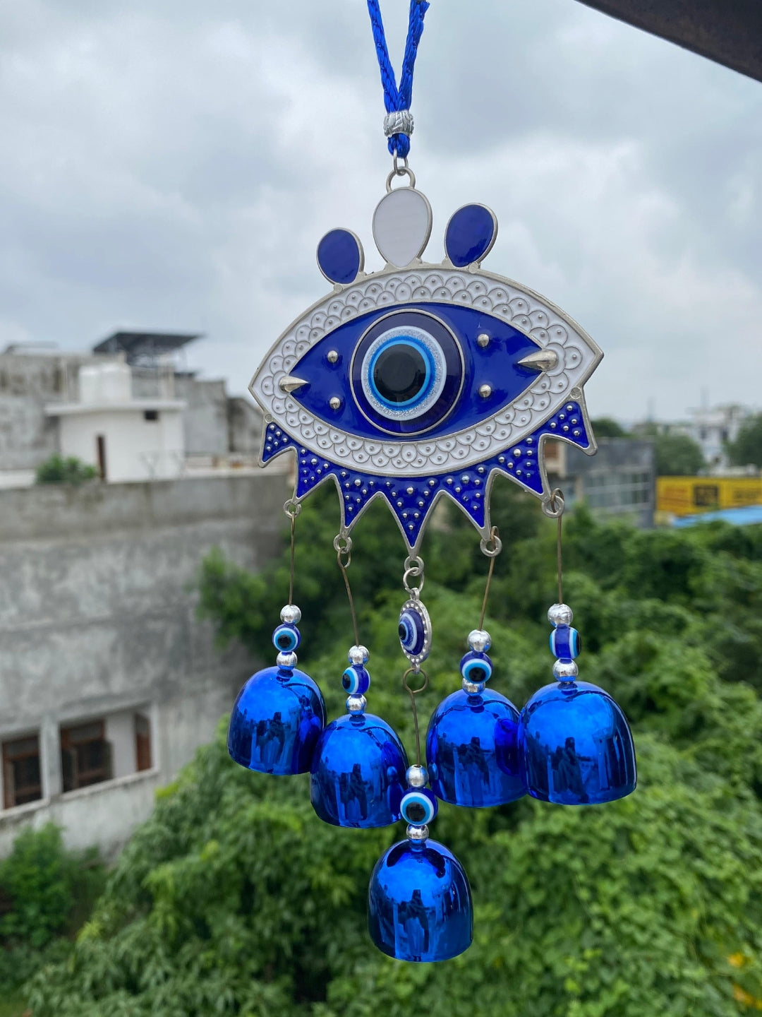 Decorative evil eye with blue accents and bells against a cityscape background
